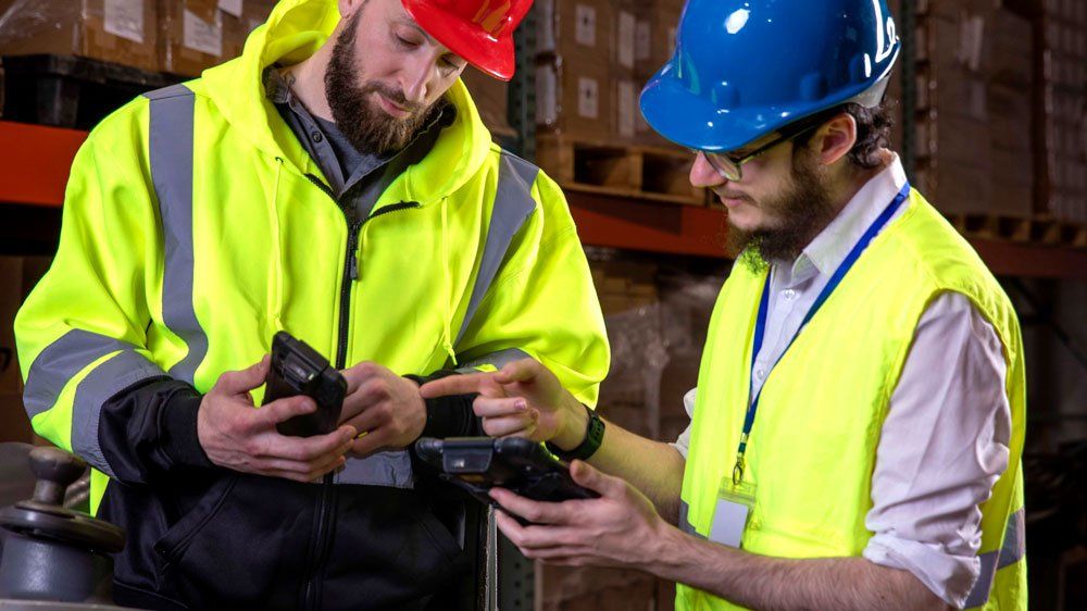 Two workers in warehouse comparing information on Sonim RS60