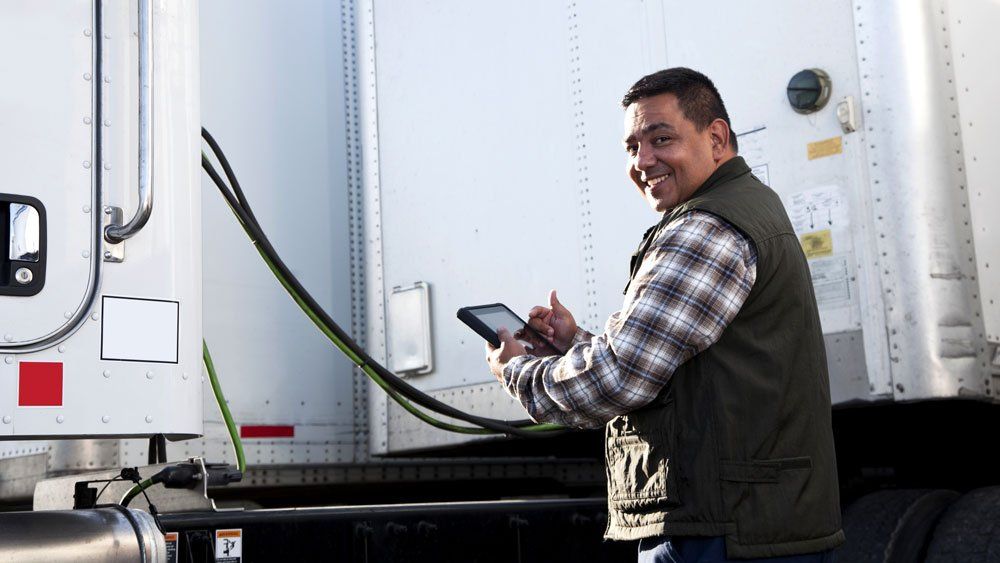 worker using mobile tablet stands in front of trucks