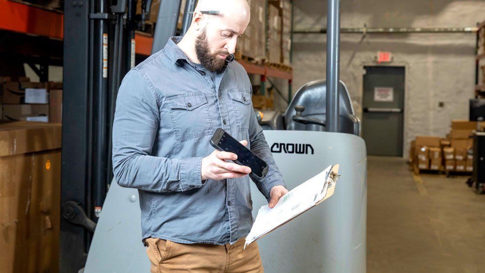 male worker in warehouse using sonim rs60 to scan clipboard