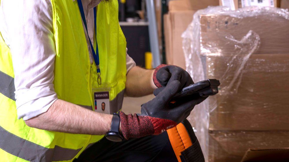 worker kneeling in warehouse uses tablet with gloves on