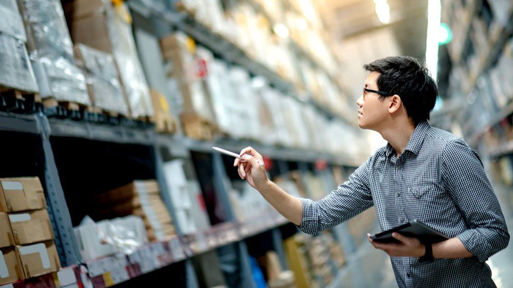 man holding tablet and stylus looks up at warehouse inventory