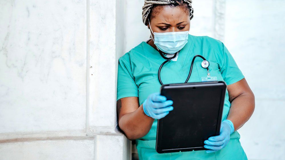 healthcare worker using tablet leans against wall