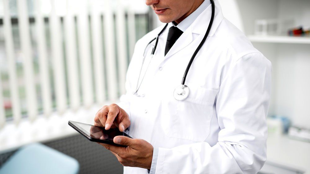 doctor in clinic wearing white coat uses tablet