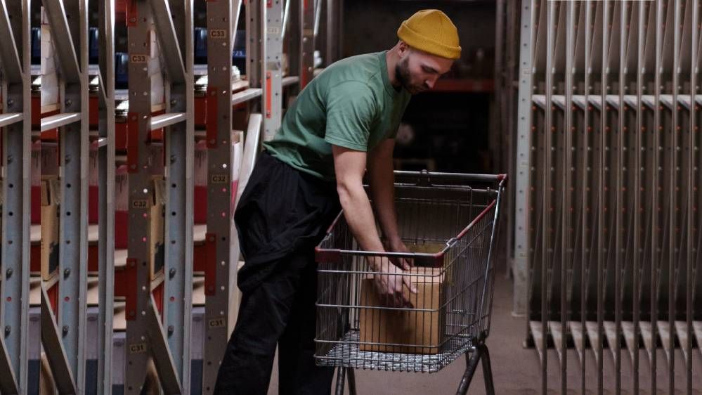 A man with hair bonnet picking a box in a cart