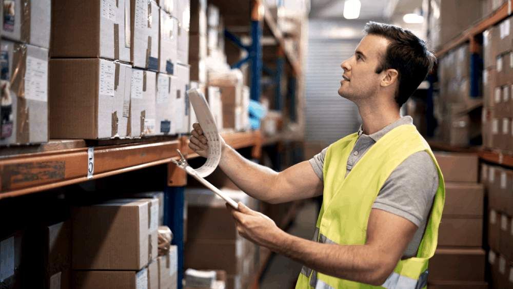 man looking at boxes with clipboard in warehouse