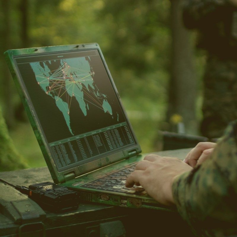 soldier in forest using rugged military laptop for strategy