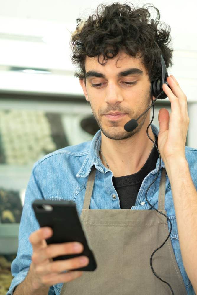 A man with curly hair is wearing headphones while looking at his phone