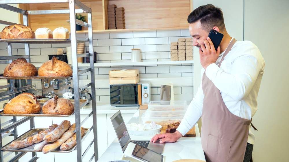 A man inside the pastry operates a laptop while calling in the phone