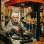 An elderly man riding a forklift while making a phone call